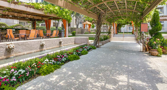 a courtyard with a pergola and flowers and chairs at La Ventura Apartments, Texas