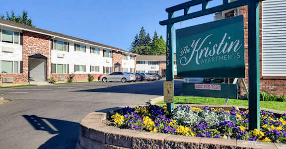 A sign for The Kristin Apartment is in front of a building.
