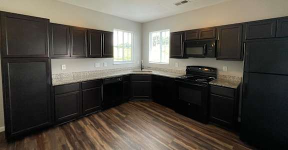 A kitchen with black cabinets and a wooden floor.