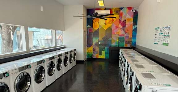 A laundromat with rows of washing machines and a colorful wall.