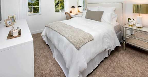 A bedroom with a large bed, a nightstand, and a window with curtains.