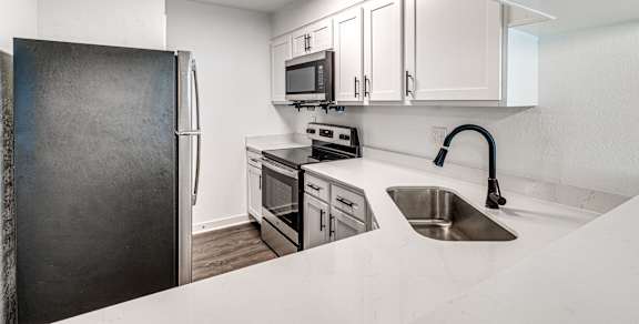 A kitchen with a black refrigerator, white countertops, and stainless steel appliances.