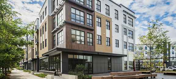 A modern multi-story building with a mix of wood and glass features a walkway in front.