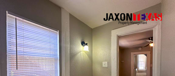 A hallway with a light switch and a window with blinds.