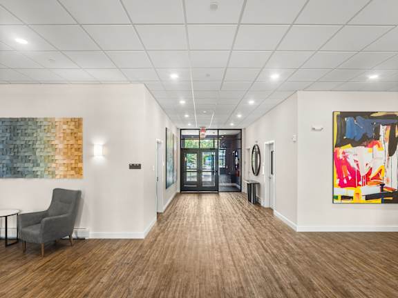 A hallway with a chair, a table, and a painting on the wall.