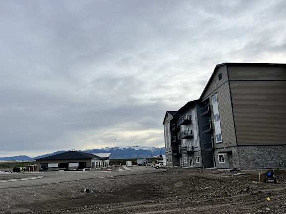A large building with a grey roof is under construction with mountains in the background.