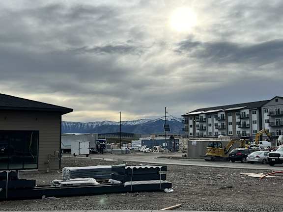 A construction site with a building and a yellow excavator in the foreground.
