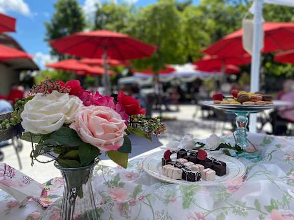 A table with a floral tablecloth and a vase of flowers is set for an outdoor meal.