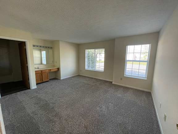 A sparsely furnished room with a carpeted floor and two windows.