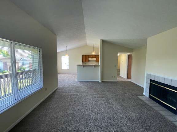A spacious living room with a fireplace and a kitchen area in the background.