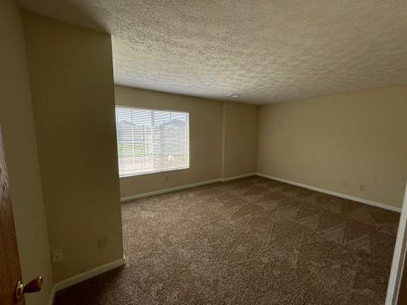A room with carpeted floor and a window letting in light.