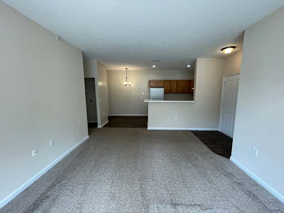 A spacious room with a carpeted floor and a small kitchenette in the corner.