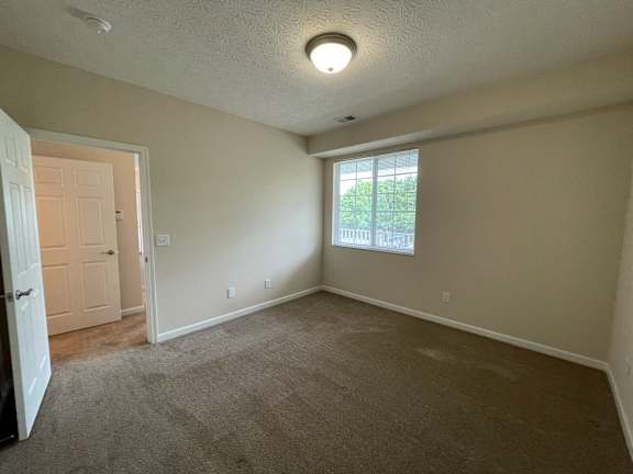 A room with a carpeted floor and a window showing trees outside. at The Legends at Steeplechase, Richwood, Kentucky