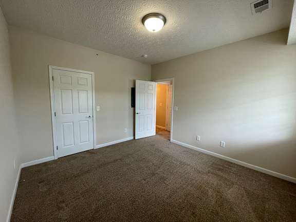 A carpeted room with a door on the left and a mirror on the right. at The Legends at Steeplechase, Richwood, KY, 41094