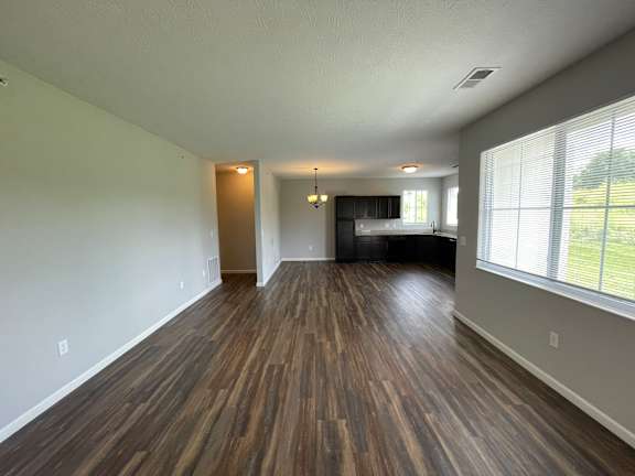 A room with wooden flooring and a kitchen in the background.