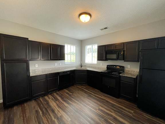 A kitchen with black cabinets and a wooden floor.