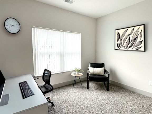A room with a desk, chair, and a picture on the wall.