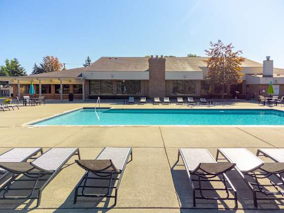 a swimming pool with chairs around it in front of a building