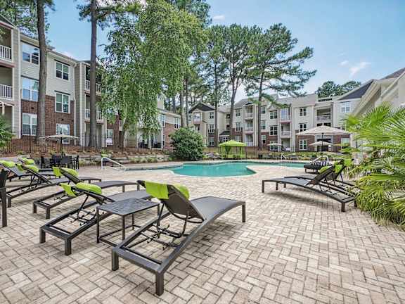 A pool surrounded by lounge chairs and trees.