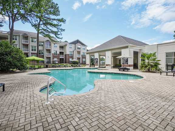 A swimming pool surrounded by a brick patio and apartment buildings.