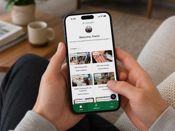 A person is holding a smartphone displaying a social media app with a welcome message and profile pictures of users.