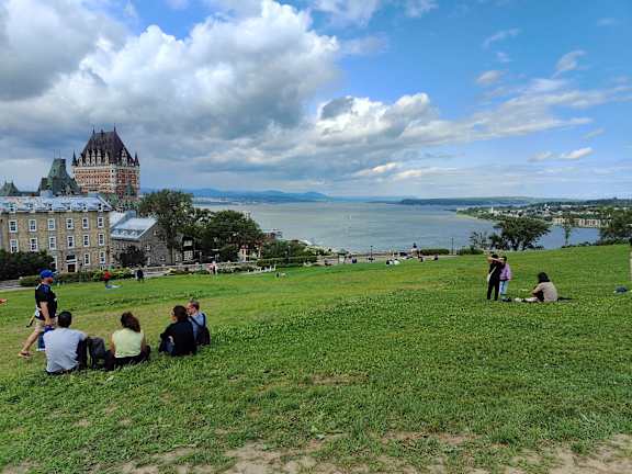 people sitting on a grassy hill overlooking the water and a castle