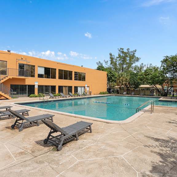 A large outdoor swimming pool with sun loungers and a building in the background at Cypress Grove, Lauderhill, 33313
