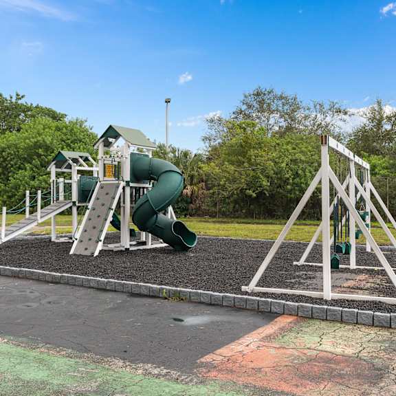 A playground with a green slide and white structure at Cypress Grove, Lauderhill, 33313