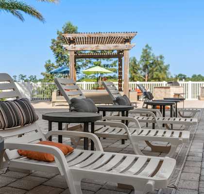 A row of white chairs with cushions are lined up on a patio at Lake Lofts at Deerwood, Jacksonville, FL, 32216