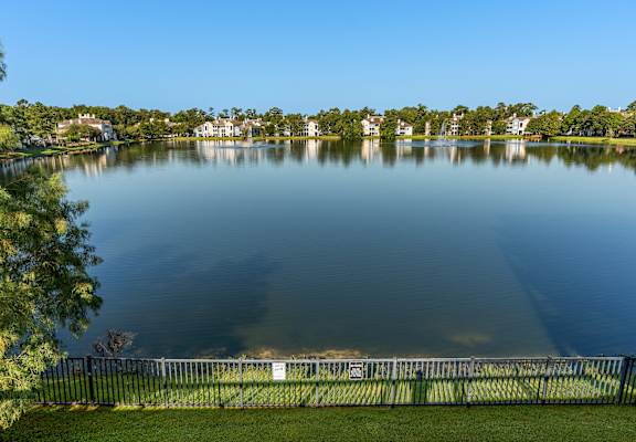 A serene lake surrounded by a fence and lush greenery under a clear blue sky at Lake Lofts at Deerwood, Jacksonville, FL, 32216