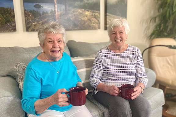 Two elderly women sitting on a couch holding mugs.