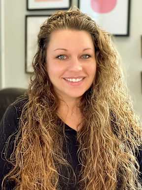 A woman with long curly hair is smiling at the camera.