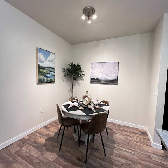 A dining room with a table set for two and two landscape paintings on the wall.