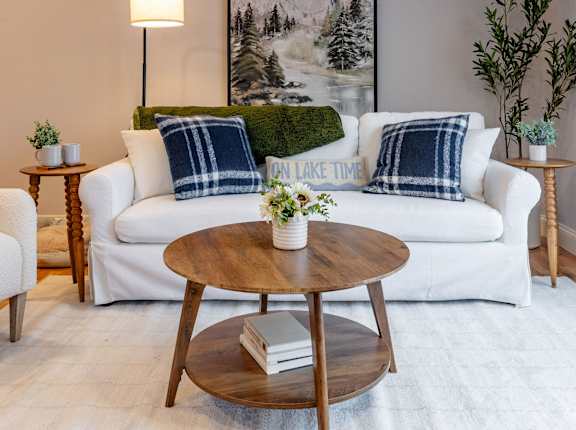 A living room with a white couch, a wooden coffee table, and a painting of a mountain landscape on the wall.