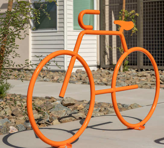 An orange bicycle sculpture is in front of a white house.