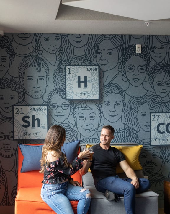 a couple sits on a couch in front of a mural of faces