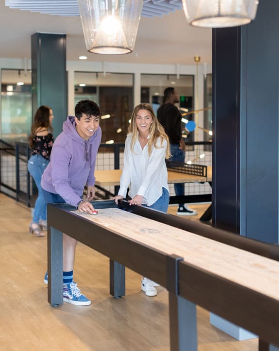 a man and a woman playing shuffleboard in a room with people in the background