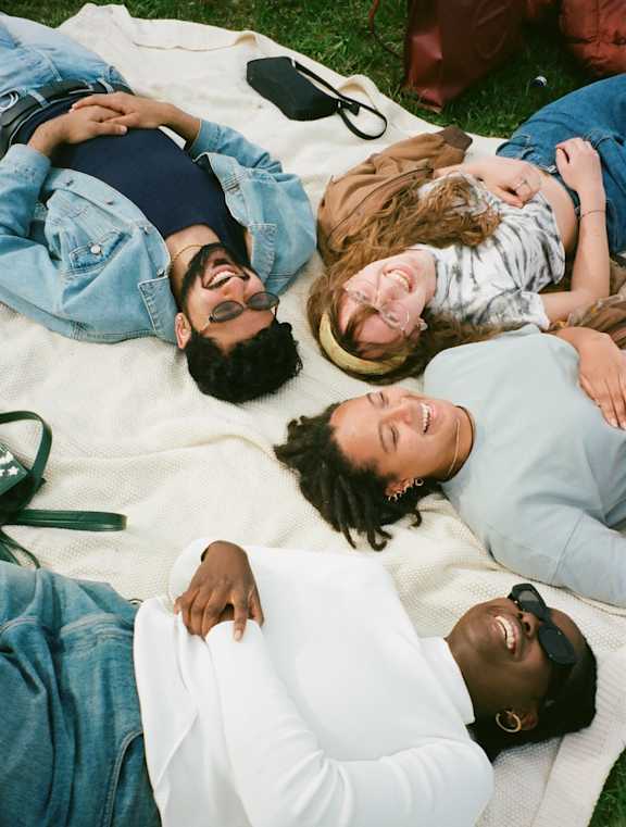 Four people lying on a blanket outdoors.