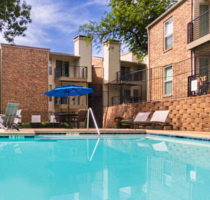 A swimming pool surrounded by chairs and umbrellas in front of nearby apartments at Canyon Creek in the Midtown neighborhood of Dallas, TX.