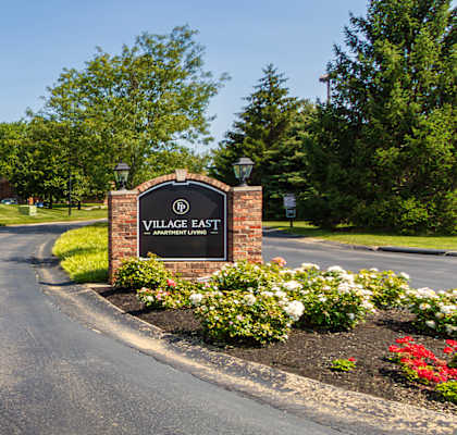 Community entrance drive with monument sign and landscaped curb appeal at Village East Apartments in Franklin