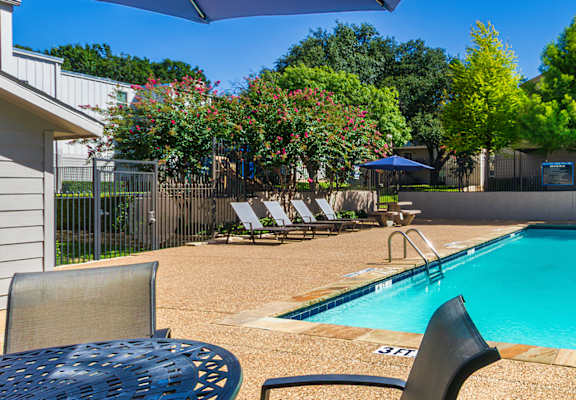 A small pool surrounded by chairs and trees.
