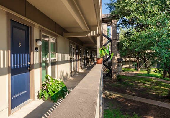 Exterior walkway with apartment doors and landscaped courtyard at Harvard Square Apartments