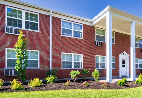 Brick apartment building with white columns and landscaped lawn at Lake of the Woods Apartments