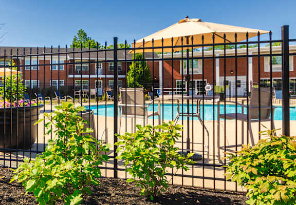 Pool entrance with black fencing, flowers, and umbrella-covered seating at Lake of the Woods Apartments