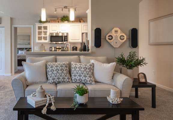 View across the Nautica living room toward the kitchen and dining areas, with a sofa, coffee table, white cabinets, and pendant lights.