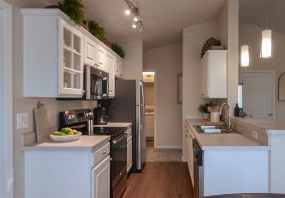 Kitchen and breakfast bar in the Nautica apartment, with white cabinetry, dark appliances, wood-style flooring, and an open connection to the living room.