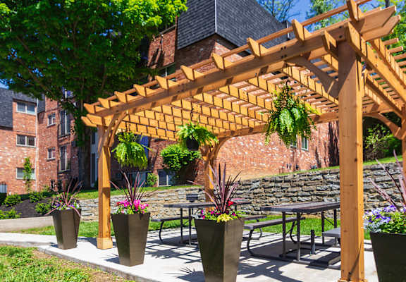 A wooden pergola with hanging plants is in front of a apartment buildings at Romaine Court Apartments in the Oakley neighborhood of Cincinnati, Ohio.