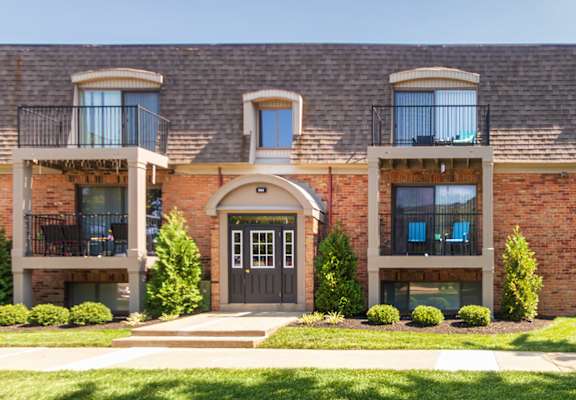 Brick apartment building with balconies, arched entry, and landscaped lawn at Village East Apartments in Franklin, Ohio