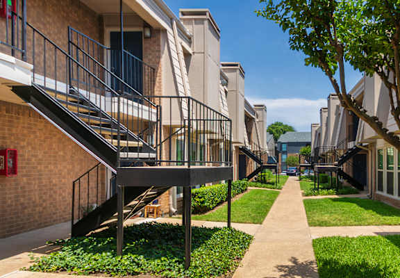 Walkway between apartment buildings with green showing landscaping at Woodbridge Apartments in Midtown, Dallas, TX.