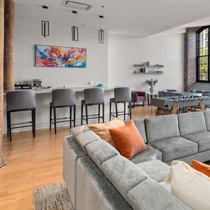 A living room with a grey couch and orange pillows.